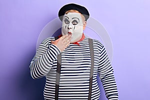 Shocked mime artist standing in disbelief closing his mouth with a palm