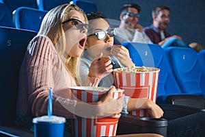 shocked multiracial women in 3d glasses with popcorn watching film together