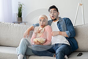 Shocked muslim couple watching thriller on TV
