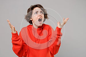 Shocked nervous young brunette woman girl in casual red hoodie posing isolated on grey wall background in studio. People