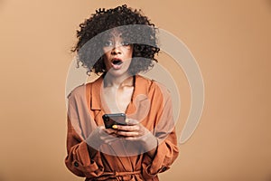 Shocked pretty african woman using smartphone and looking at camera