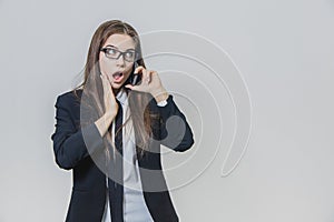 Shocked pretty businesswoman is holding a phone in her hand and talking. Attractive lady is looking stunning. Girl is