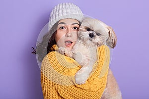 Shocked pretty younggirl holding dog and looking directly at camera with opened mouth, attractive female expressing astonishment