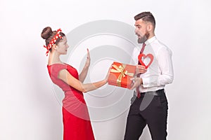 Shocked sad woman showing stop gesture to man with present and heart, female saying no refuse a gift