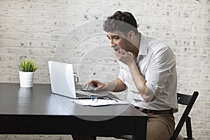 Shocked businessman after reading bad news in laptop about his business sits at the desk with documents