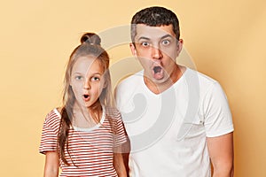 Shocked scared father and daughter wearing casual t-shirts standing isolated over beige background looking at camera with opend