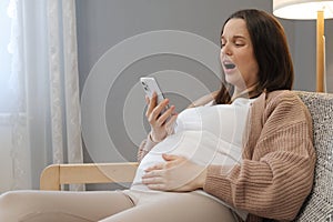 Shocked scared pregnant woman in labor calling hospital screaming from strong terrible pain holding smartphone in hands needs help