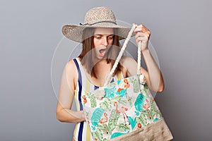 Shocked scared woman wearing striped one-piece swimsuit and straw wide brim hat posing isolated on gray background looking at her