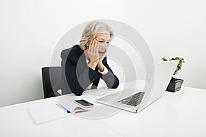 Shocked senior businesswoman using laptop at desk in office