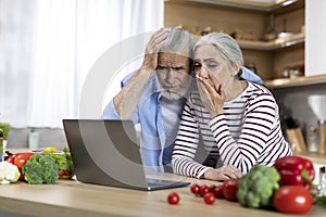 Shocked senior couple looking at laptop screen in kitchen