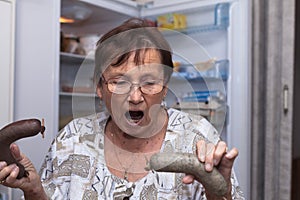 Shocked senior woman holding pork liver sausages