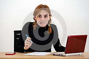 Shocked serious young office worker woman sitting behind working desk with laptop computer, cell phone and notebook