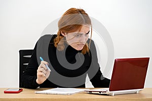 Shocked serious young office worker woman sitting behind working desk with laptop computer, cell phone and notebook