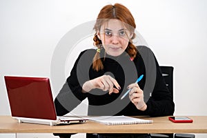 Shocked serious young office worker woman sitting behind working desk with laptop computer, cell phone and notebook