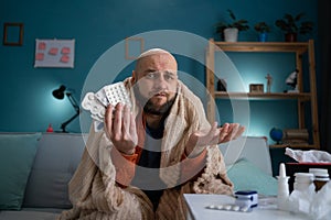 Shocked sick man at home holding blisters of pills looking at camera.