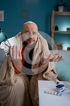 Shocked sick man at home holding blisters of pills looking at camera