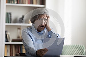 Shocked stressed middle aged woman looking at paper document.