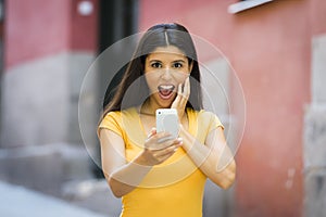 Shocked and surprised attractive young latin woman texting and talking on her smart cell phone