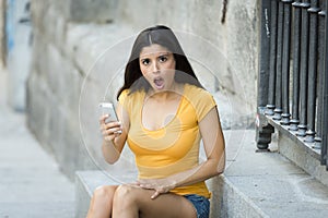 Shocked and surprised attractive young latin woman texting and talking on her smart cell phone