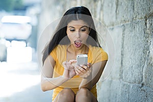 Shocked and surprised attractive young latin woman texting and talking on her smart cell phone