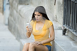 Shocked and surprised attractive young latin woman texting and talking on her smart cell phone