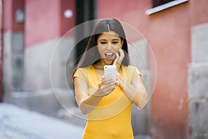 Shocked and surprised attractive young latin woman texting and talking on her smart cell phone