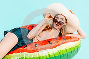 Shocked surprised girl dressed in a swimsuit and a summer hat, sitting on an inflatable ring, resting on a blue background