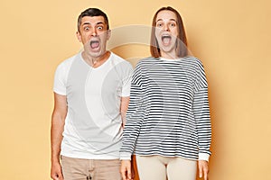 Shocked surprised man and woman wearing casual clothing standing isolated over beige background expressing fear and being scread