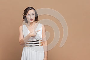 Shocked surprised middle aged woman with wavy hair pointing away at copy space for advertisement