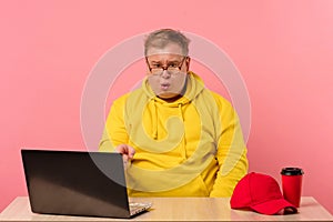 Shocked surprised plump man in yellow staring at laptop monitor with open mouth.