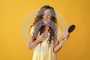 shocked teen girl with long curly hair holding comb hairbrush for combing, daily habits