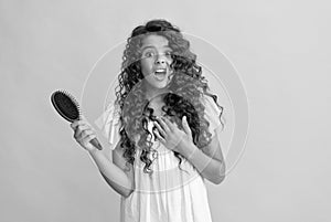 shocked teen girl with long curly hair holding comb hairbrush for combing, daily habits