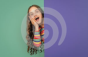 shocked teen kid behind blank blue paper with copy space for advertisement