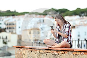 Shocked teenage girl checking phone on vacation