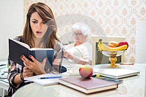 Shocked teenage girl reading book in front of her grandmother at home.