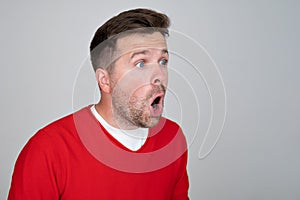 Shocked unshaven man expressing surprise on camera isolated over gray background
