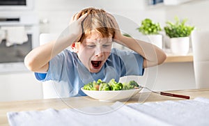 Shocked and upset little boy because he has to eat broccoli for dinner, which he doesn't like