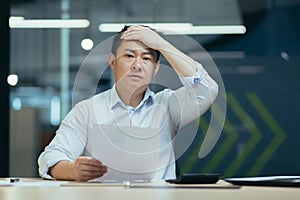 Shocked and upset young male Asian student holds a document in his hands. exam results, bill