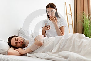 Shocked Wife Reading Message On Cheating Husband& x27;s Smartphone In Bedroom