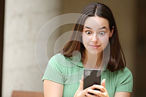 Shocked woman checking cell phone in the street