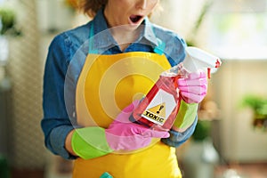 Shocked woman with cleaning agent reading instruction