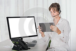 Shocked woman with headset in the office using digital tablet and computer screen is blank for copy space