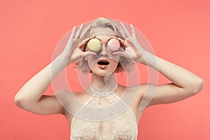 shocked woman in lace bra holding two macarons in front of eyes, isolated on red