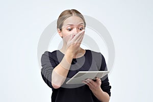 Shocked woman looking at digital tablet with surprise and shock over gray background