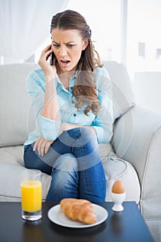 Shocked woman on the phone sitting on sofa