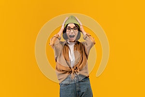 Shocked woman raising hands up and touching head over yellow studio background, emotional lady expressing amazement