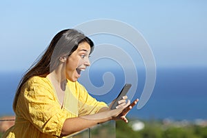 Shocked woman reads exciting news on phone in a balcony