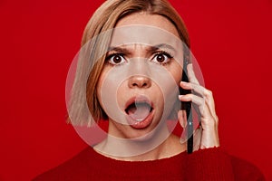 Shocked woman screaming while talking on smartphone isolated over red background
