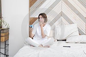 Shocked woman sitting on the bed and holding alarm clock