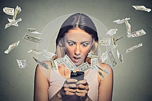 Shocked woman using smartphone dollar bills flying away from screen